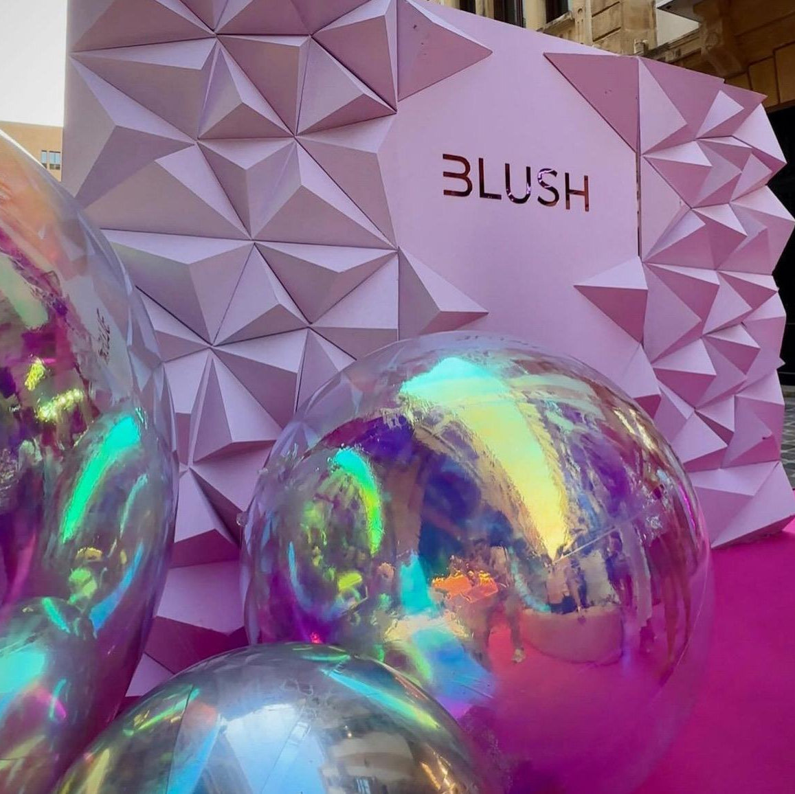 Iridescent spherical objects in front of a pink geometric-patterned 'Blush' box.