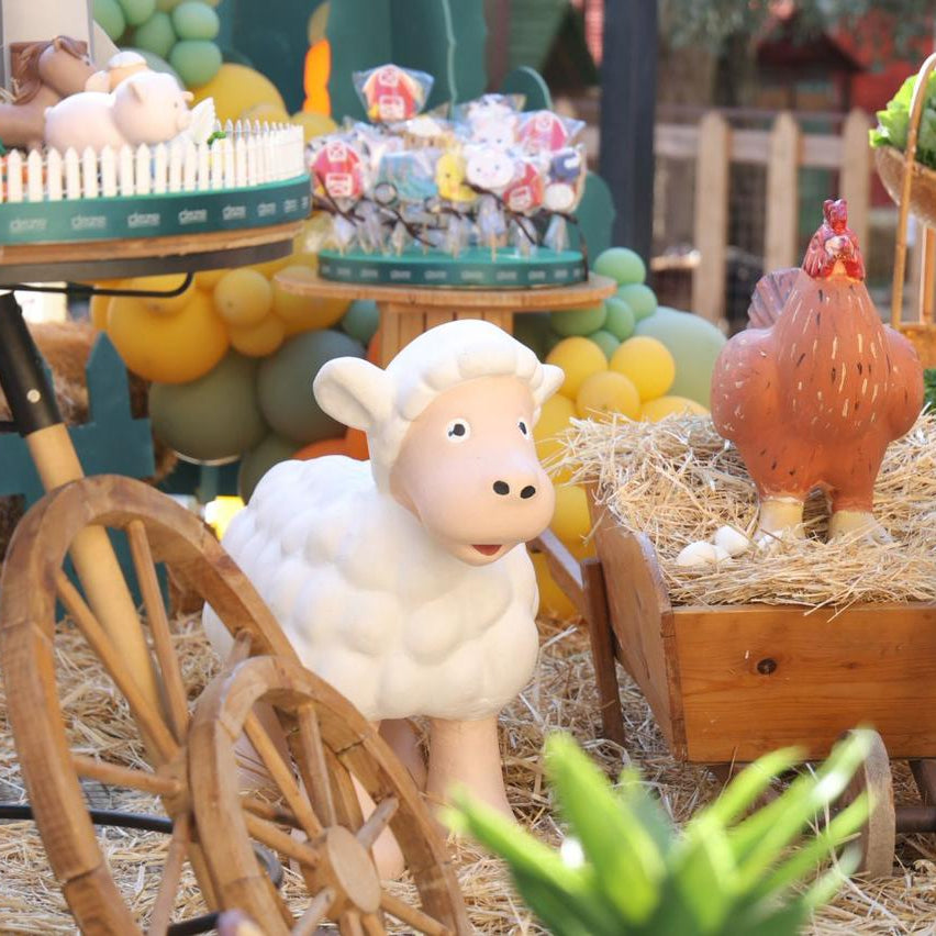 Toy sheep and rooster with a wooden cart and hay in a playful setting.