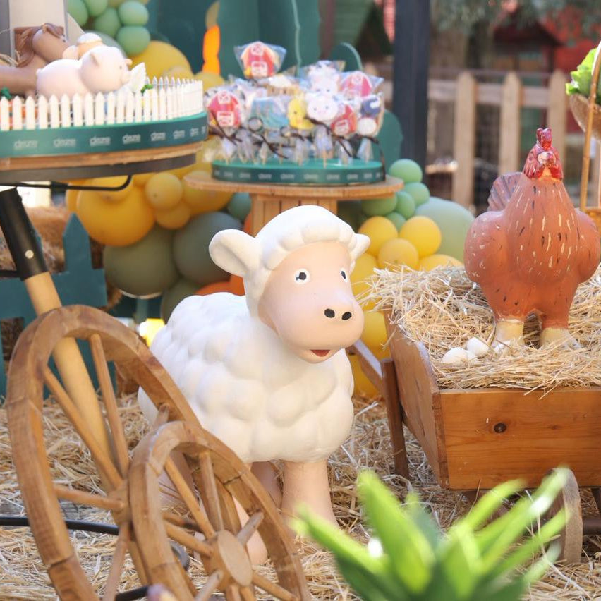Toy sheep and rooster with a wooden cart and hay in a playful setting.