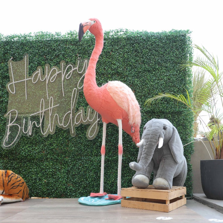Decorative flamingo and elephant with 'Happy Birthday' sign against a green hedge.