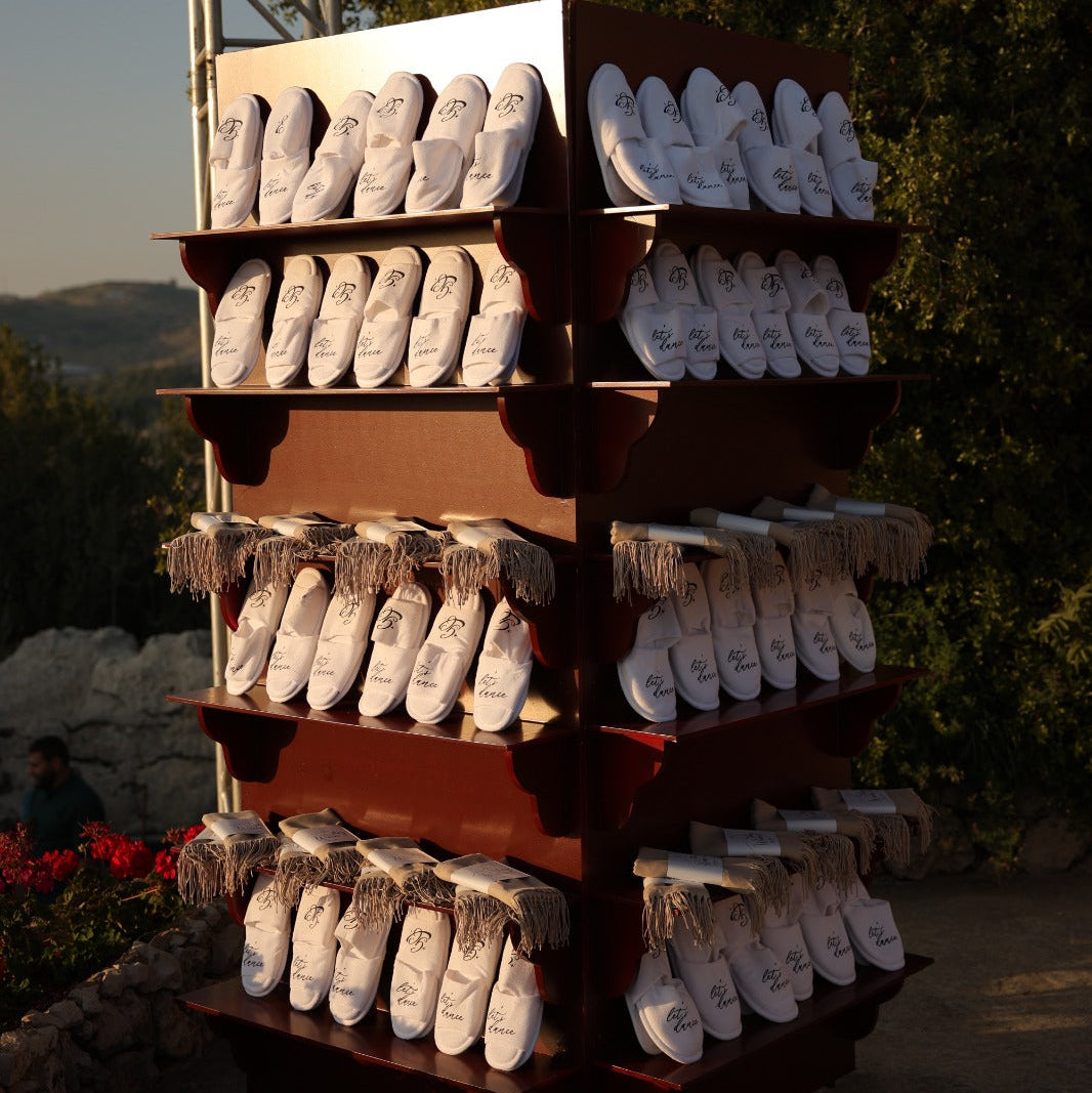 Display of white shoes on a wooden rack outdoors with trees and mountains in the background.