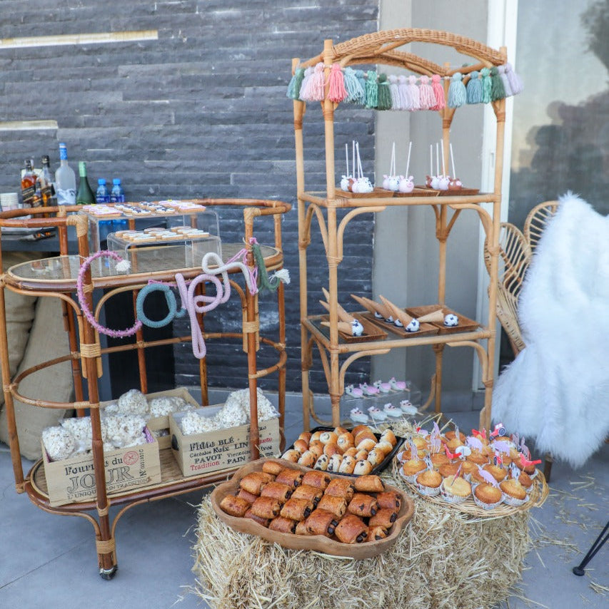Outdoor setting with a bar cart, hay bale, and food display against a stone wall.