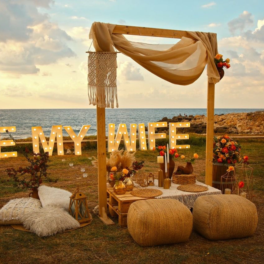 Decorated outdoor setting with 'Be My Wife' sign by the ocean