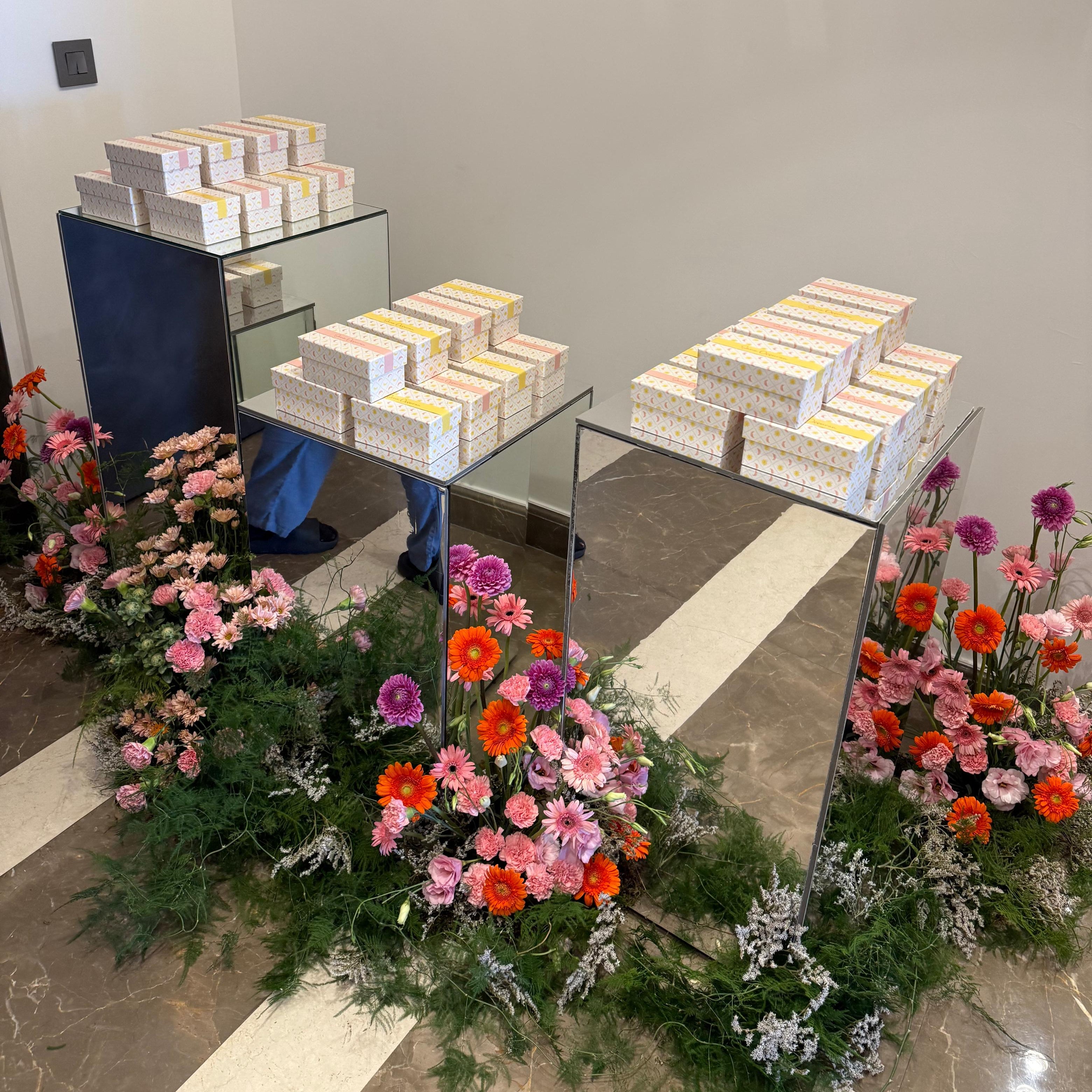 Floral arrangements and boxes on a glass table in an indoor setting