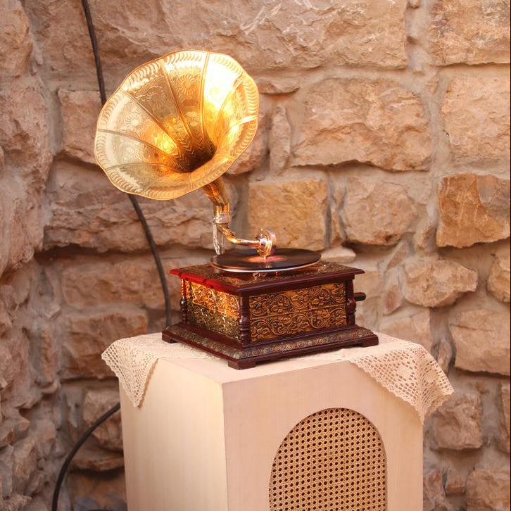 Vintage-style gramophone on a wooden stand against a stone wall.