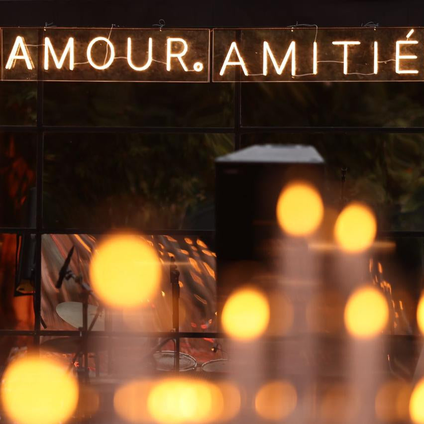 Decorative sign with 'ÂME. AMOUR. AMITIÙ' text above blurred lights and people.