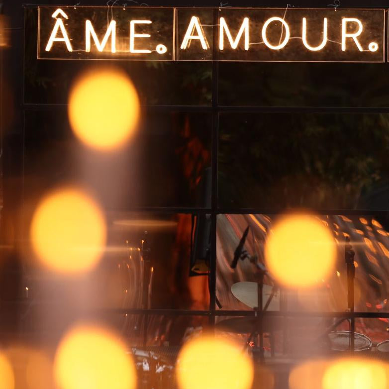 Decorative sign with 'ÂME. AMOUR. AMITIÙ' text above blurred lights and people.
