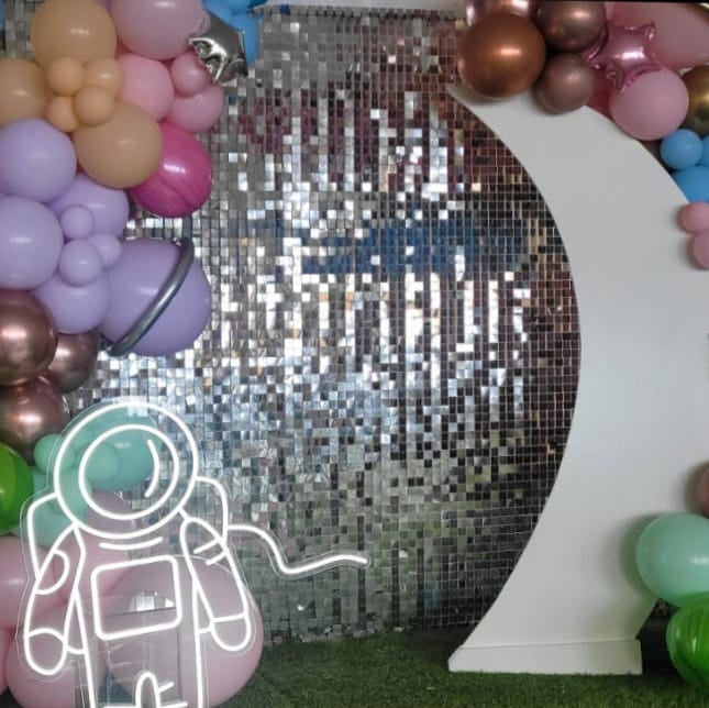 Decorative arch with balloons and a neon astronaut sign in front of a glittery backdrop