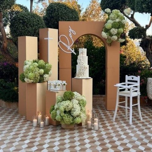 Wedding setup with a cake on a stand, flowers, and candles in an outdoor setting.
