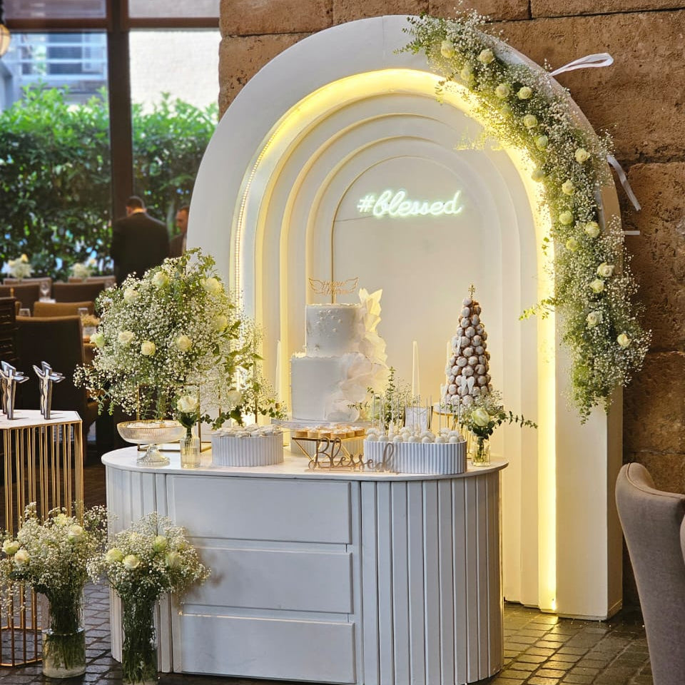 Decorative setup with a cake and floral arrangements in front of a neon sign.
