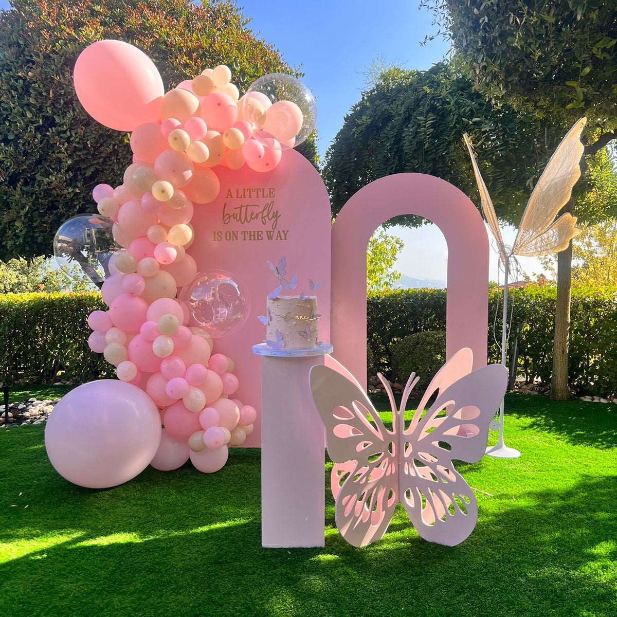 Pink balloon arch with a butterfly design and cake for a birthday party.