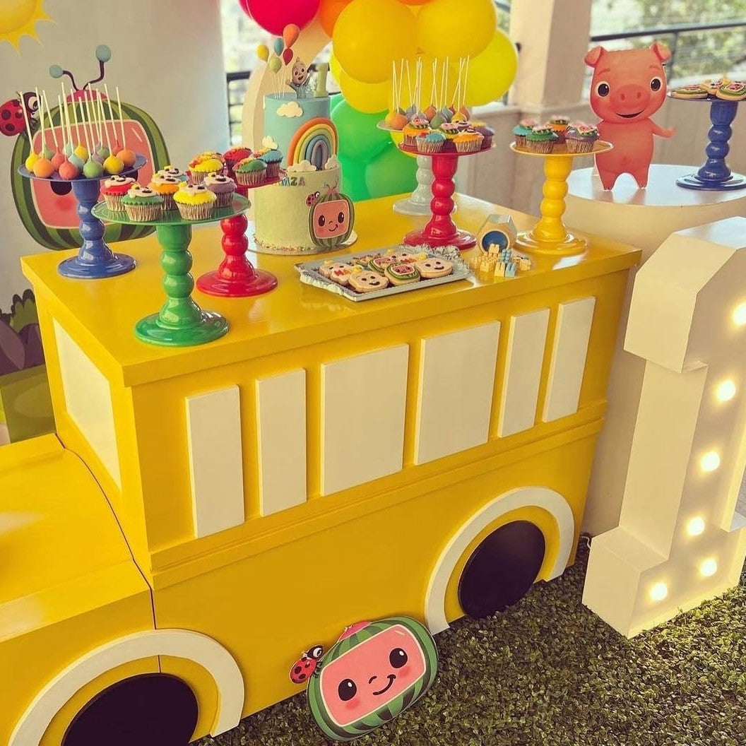 Yellow toy bus with colorful decorations and treats on a table. Cocomelon bus