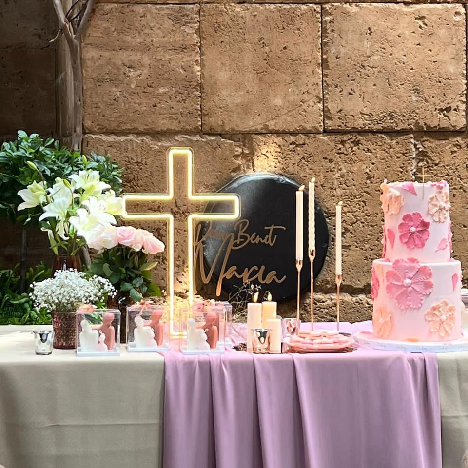 Decorated table with a cake, flowers, and a neon sign against a stone wall.