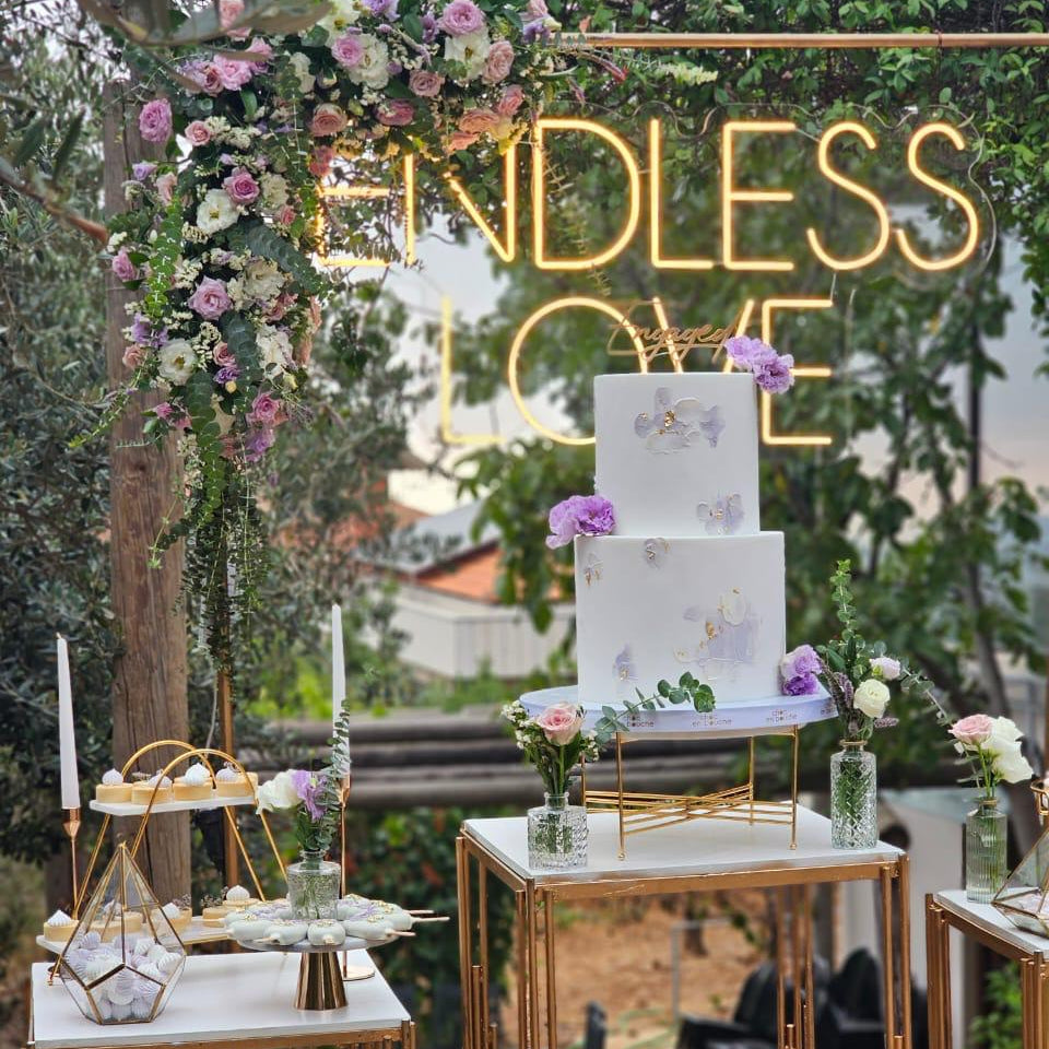 Wedding setup with a cake, floral decorations, and 'Endless Love' sign outdoors.
