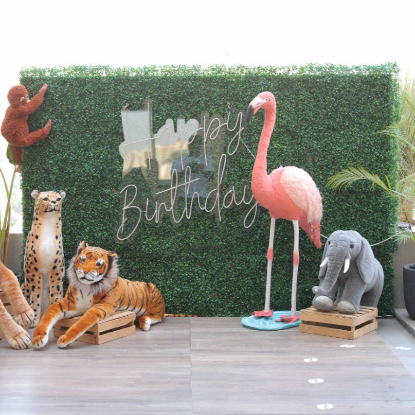 Plush animals including a flamingo, tiger, and elephant in front of a 'Happy Birthday' sign with a green textured backdrop.