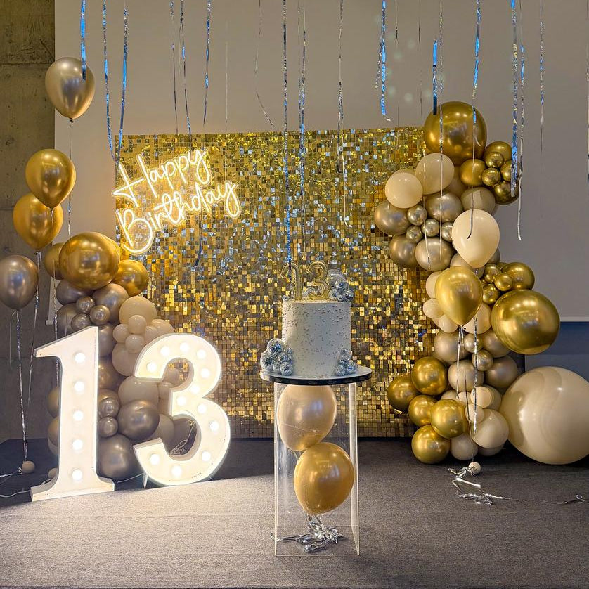 Decorative setup with balloons, a cake, and a 'Happy Birthday' sign in a room.