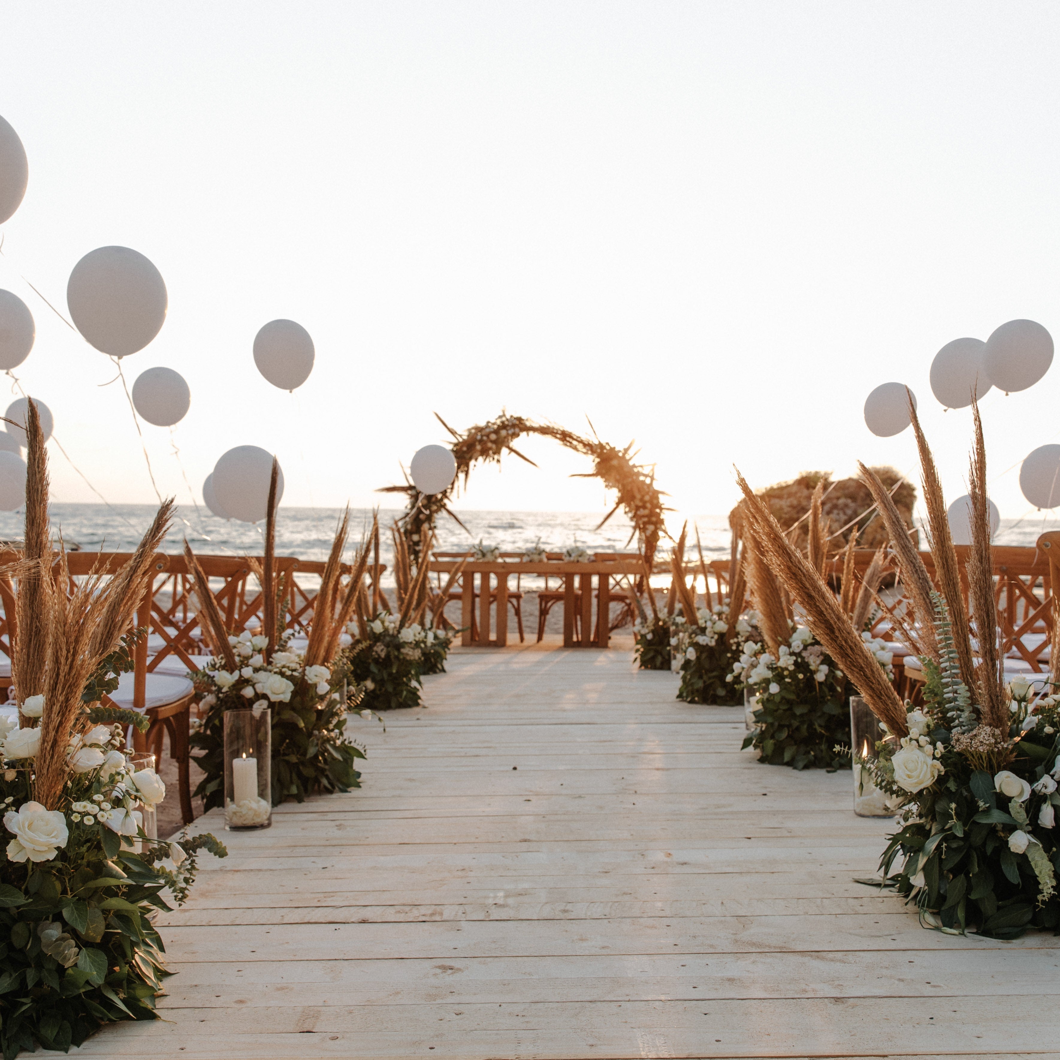 Decorative outdoor setting with balloons, wooden arch, and floral arrangements on a wooden deck.