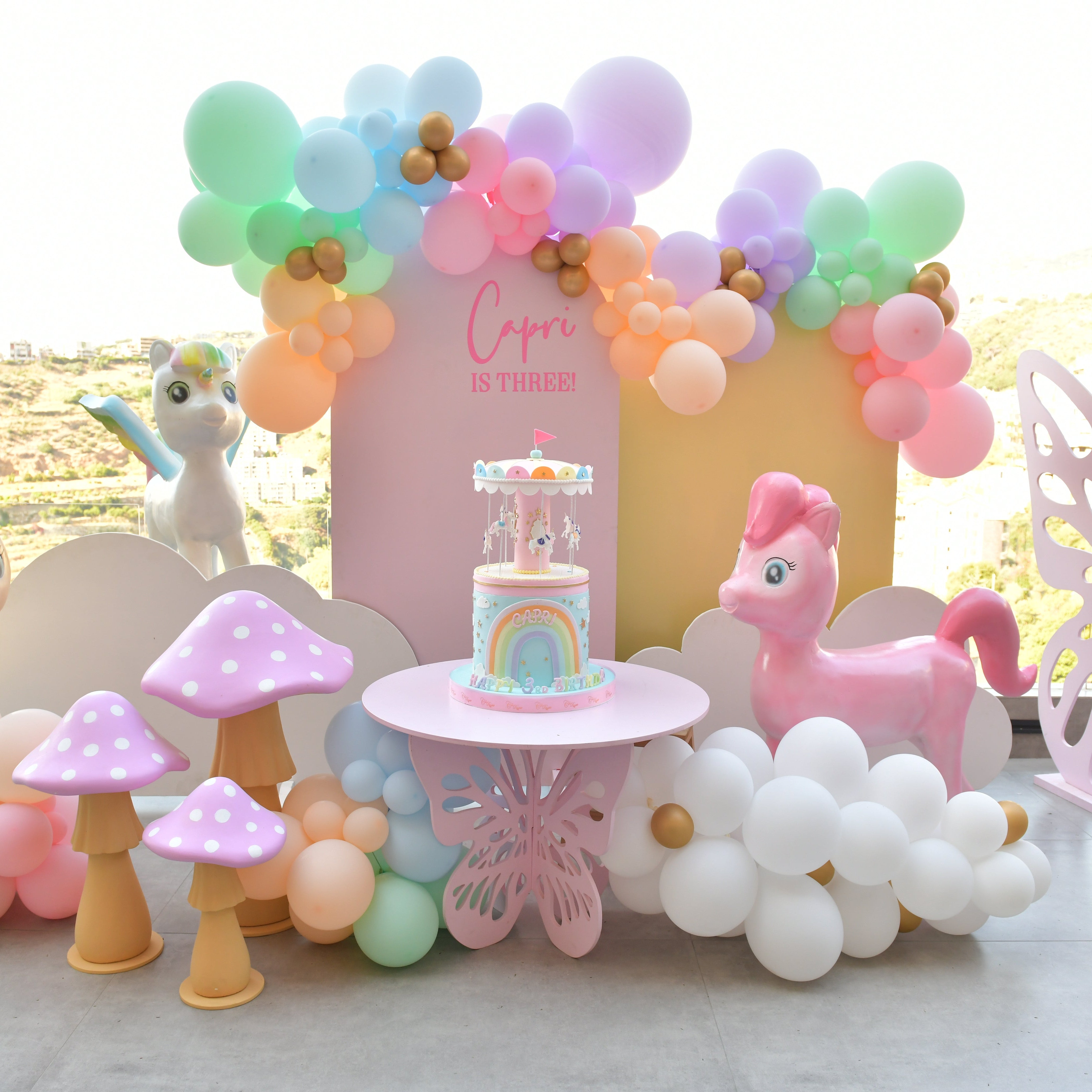 Children's birthday party setup with balloons, a cake, and toys on a table.