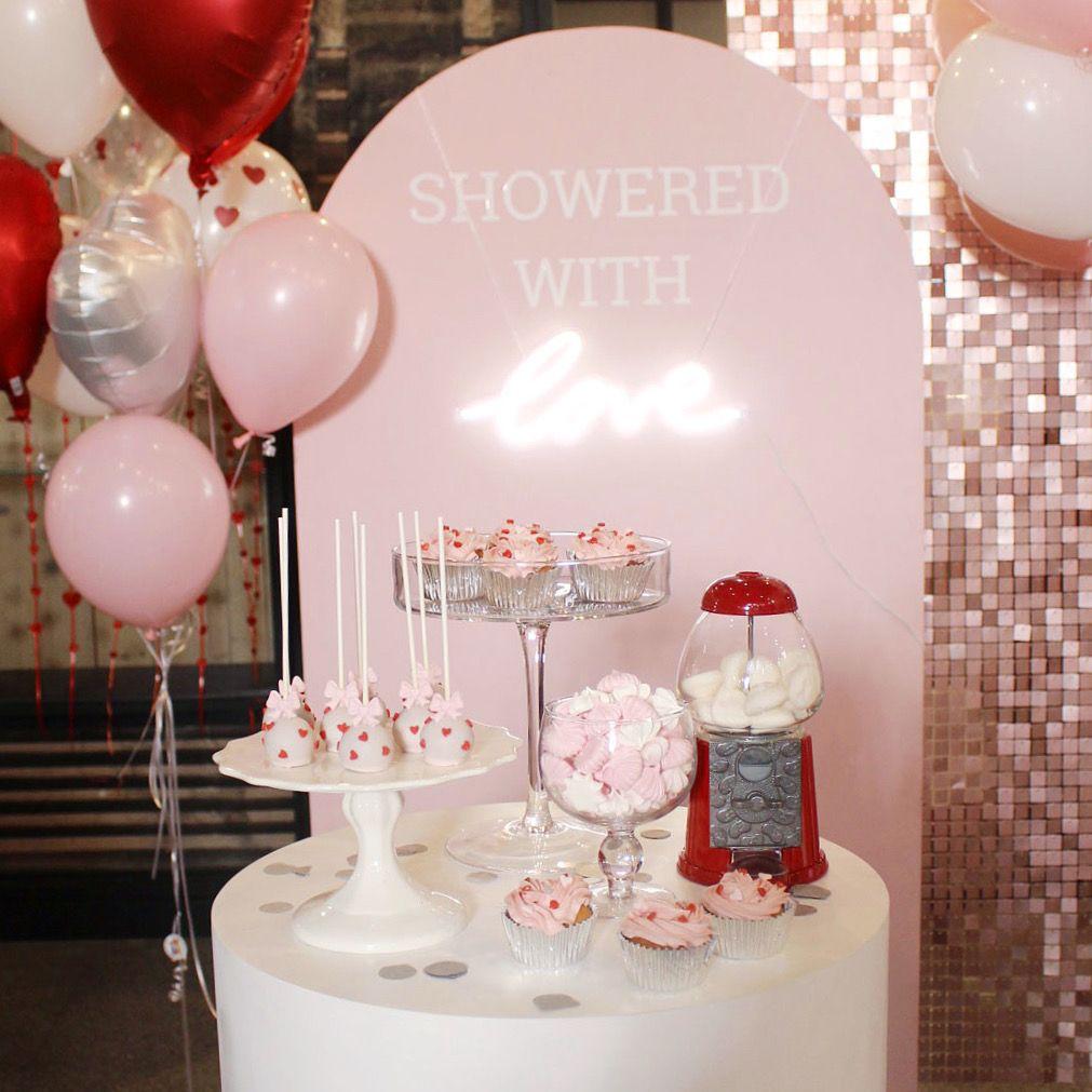 Decorative setup with balloons, candy, and 'SHOWERED WITH' text on a pink arch.