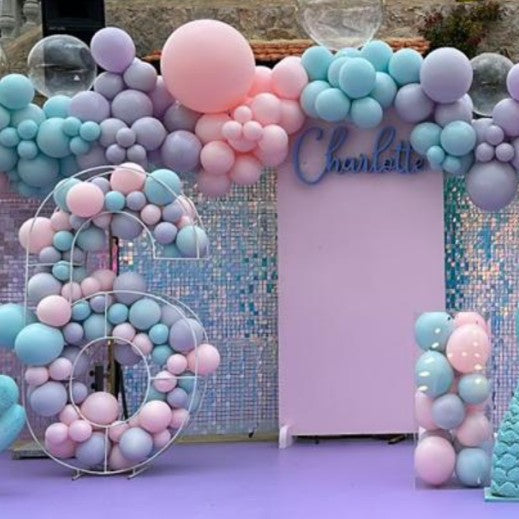Decorative balloon arch with pastel colors and a mermaid figure on a purple floor.