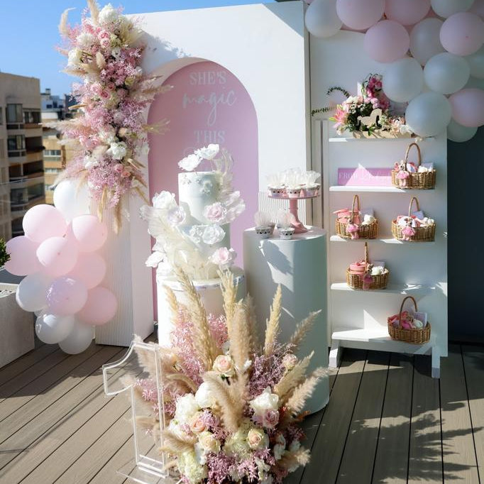 Decorative setup with flowers, balloons, and a cake on a wooden deck.