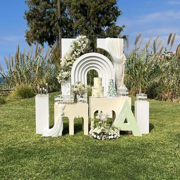 Decorative outdoor setup with arch, cake, and floral arrangements on a grassy area for a family event.
