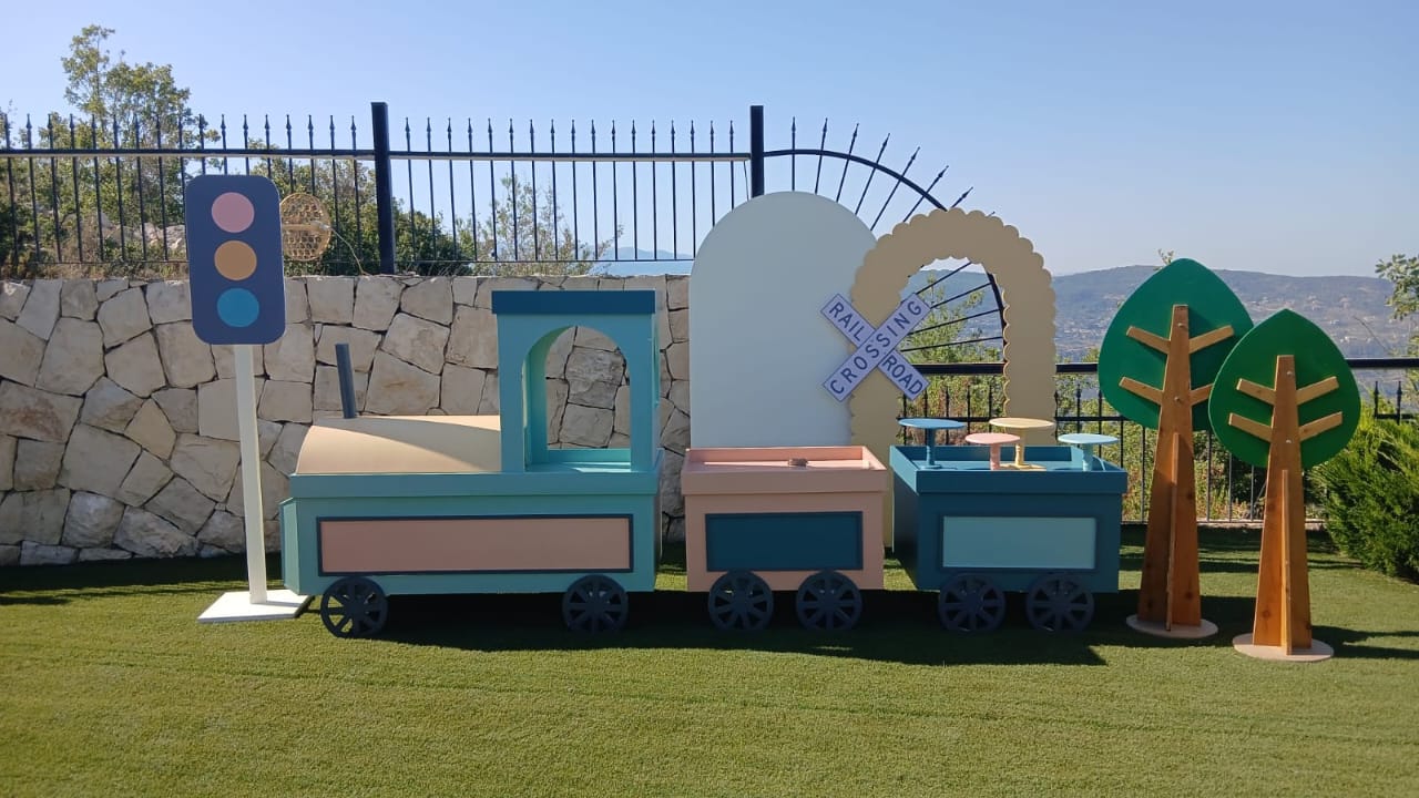 Children's play set with a toy train table, traffic lights, and trees on grass.
