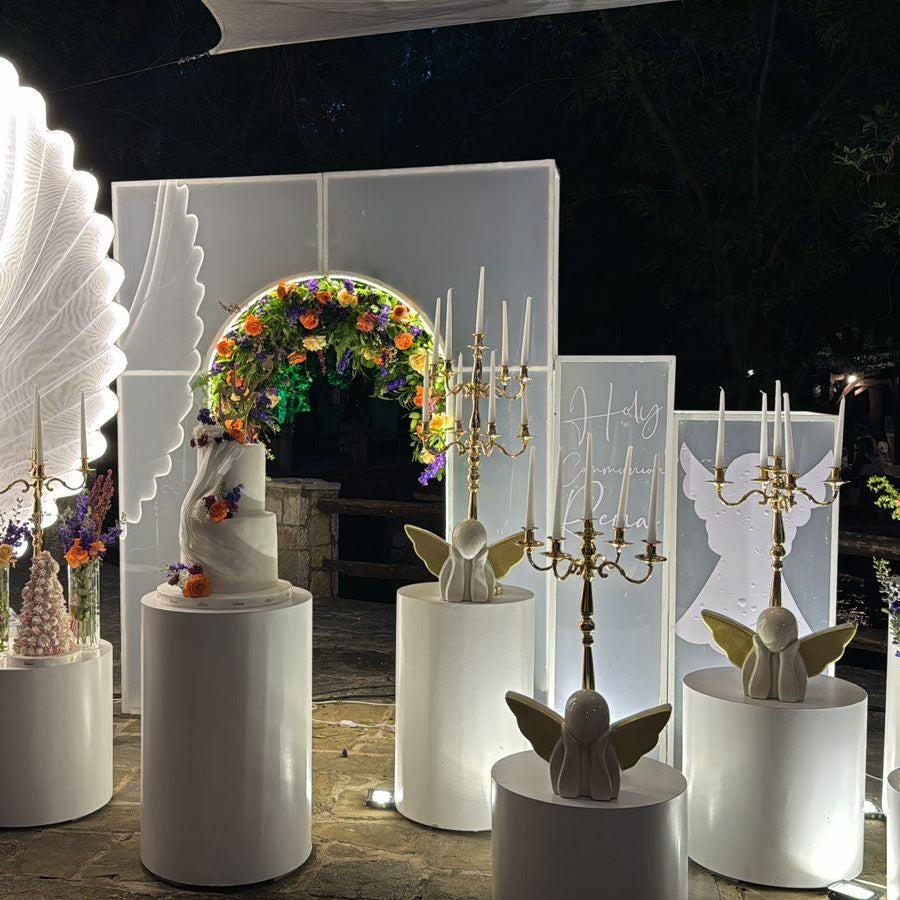 Decorative setup with candelabras, floral arrangements, and illuminated wings in a dark setting.