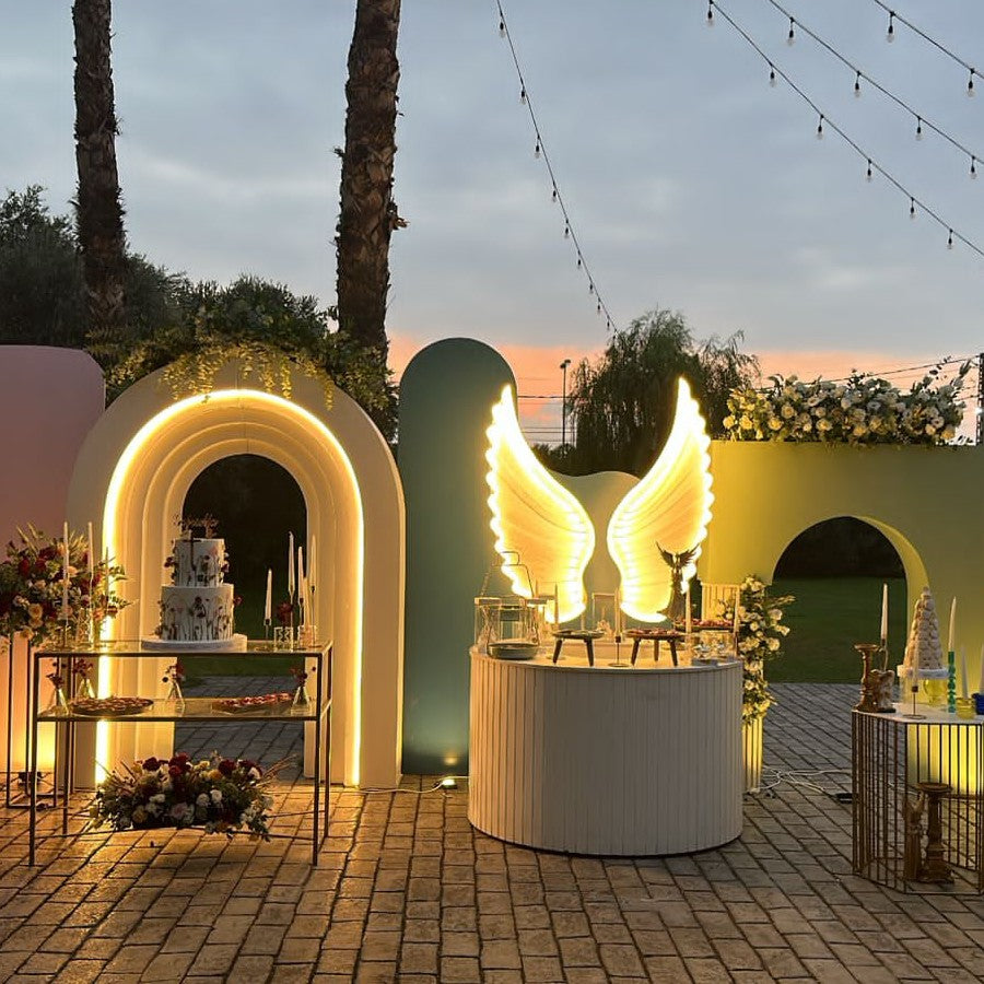 Decorative setup with arches, flowers, and a cake under a sunset sky.