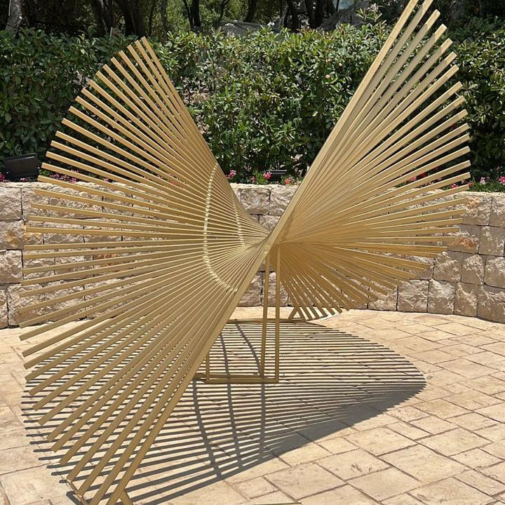 Gold metal sculpture on a stone patio with greenery in the background