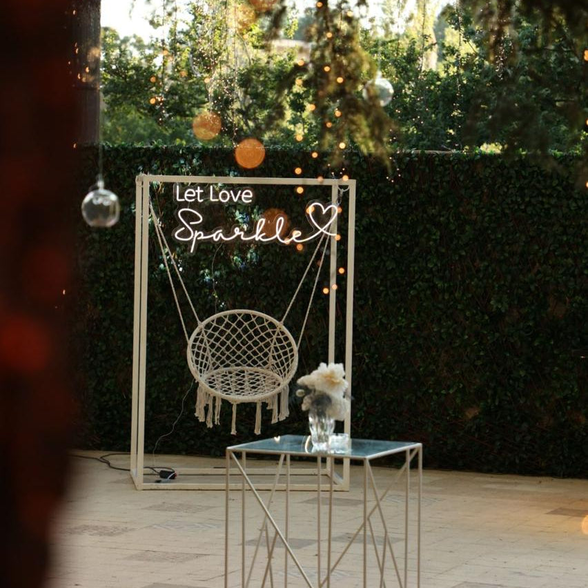 Decorative setup with a swing chair and 'Let Love Sparkle' sign in an outdoor setting.