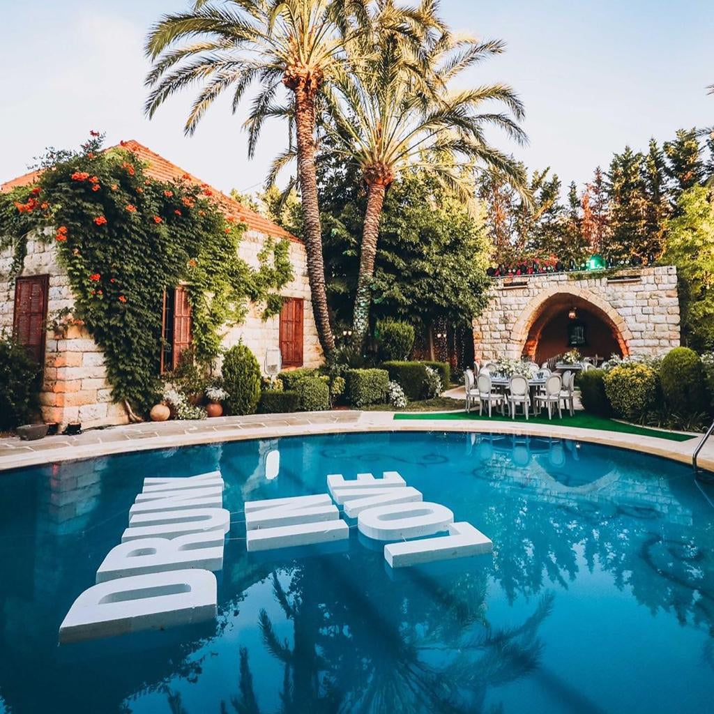 Pool area with palm trees, lounge chairs, and 'DRIVE' sign in a scenic outdoor setting.