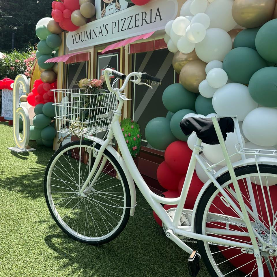 Decorative bicycle with balloons and a sign for Youmna's Pizzeria in an outdoor setting.