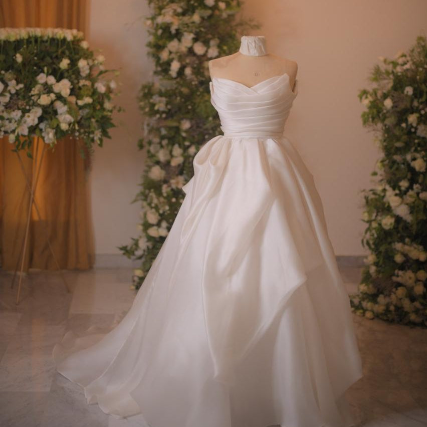 White wedding dress on a mannequin with floral decorations and a chandelier in the background.