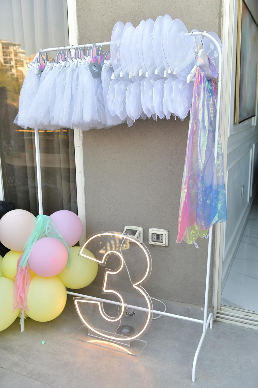 Decorative setup with white tulle, colorful balloons, and a neon number '3' on a stand.