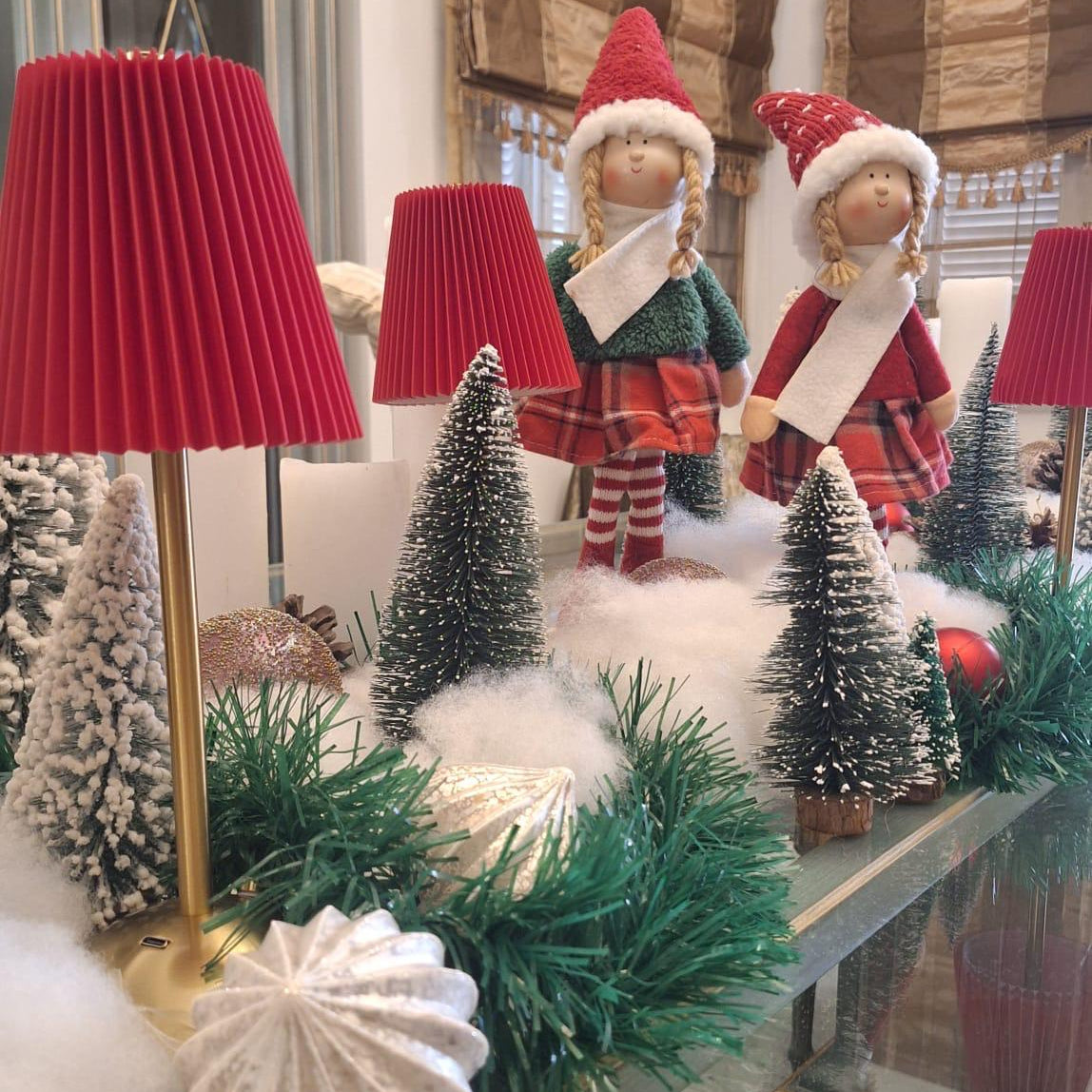 Decorative Christmas scene with red lampshades, Christmas trees, and figures in a room.