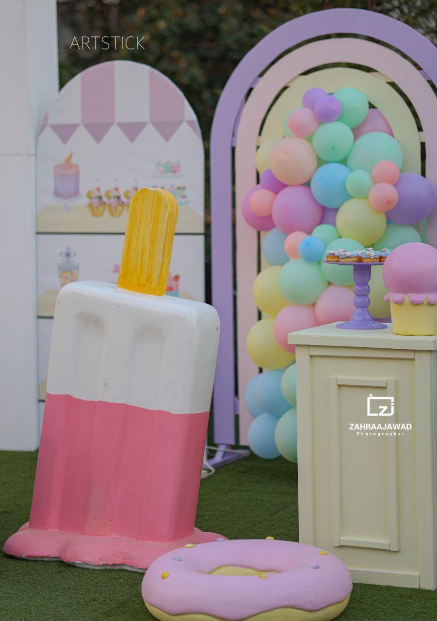 Pastel-colored ice cream and donut props with a colorful balloon arch in the background.
