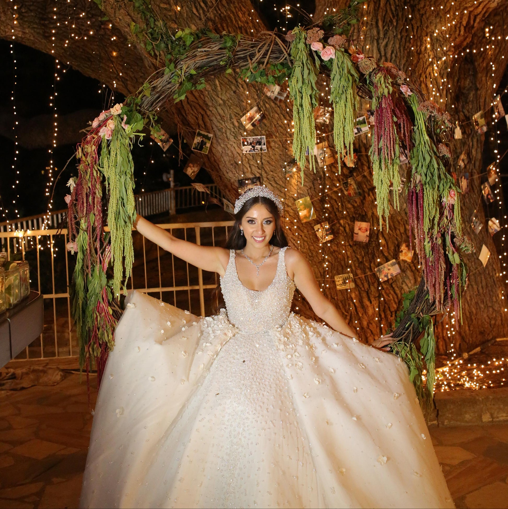 Woman in a wedding dress standing under a decorated archway with string lights at night.