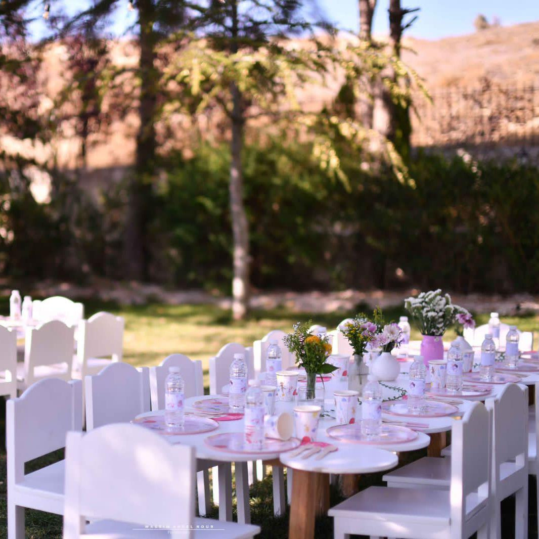 Outdoor wedding setup with white tables and chairs in a natural setting.