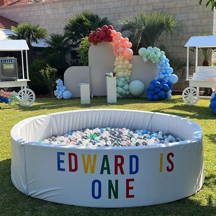ball pit for kids' birthday, colourful balloons, and decorations on a grassy area.