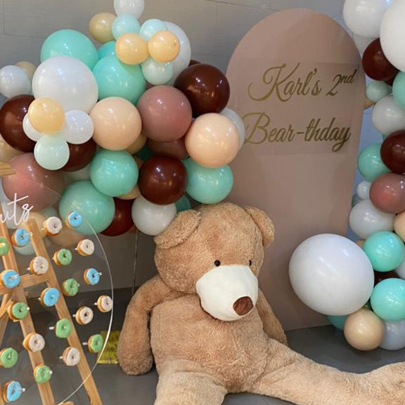 Teddy bear and balloon arch with 'Karl's 2nd Bear-thday' sign on a tiled floor.