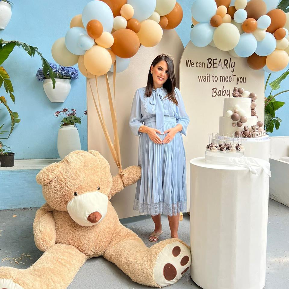 Baby shower setup with a large teddy bear, balloons, and a cake with a baby bear design.