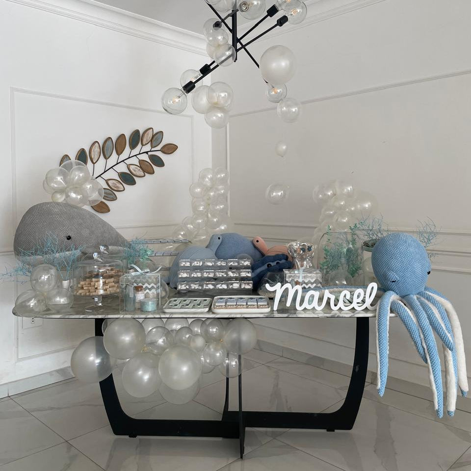 Decorative setup with a chandelier, whale, octopus, and 'Marcel' sign on a glass table.