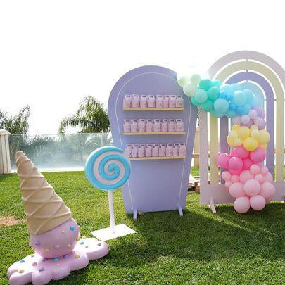 Pastel-themed candyland setup with balloons, candy decorations, and a cake on grass.