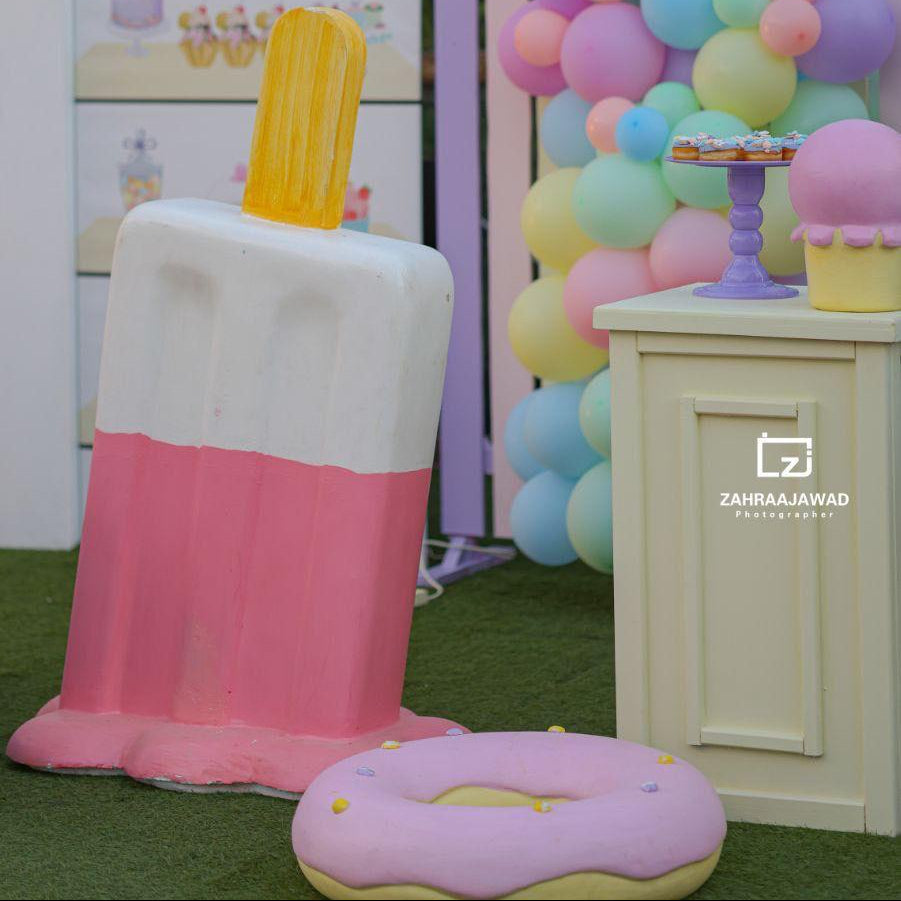 Pastel-colored ice cream and donut props with a colorful balloon arch in the background.