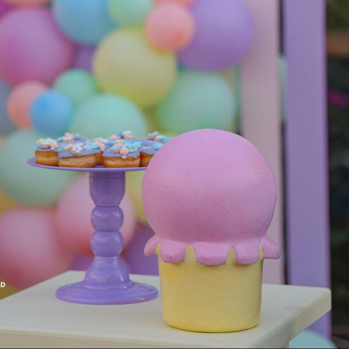 Pastel-colored balloon arch with a dessert stand and ice cream cone decoration against a blurred background.