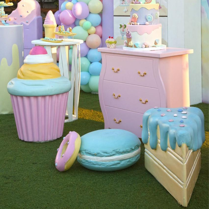 Pastel-colored playset with cupcake and cookie furniture, balloons, and small cakes on a grassy area.