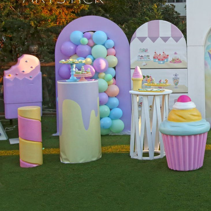 Pastel-colored inflatable decorations resembling ice cream cones, candy bars, and other sweets on a grassy outdoor setting.