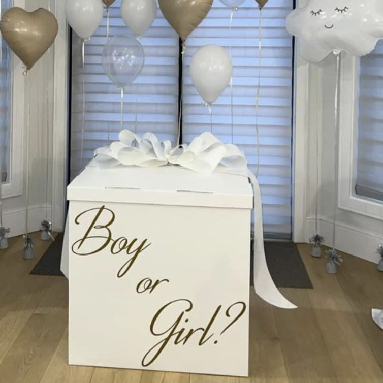 Decorative setup for a baby gender reveal party with balloons and a box labeled 'Boy or Girl?'