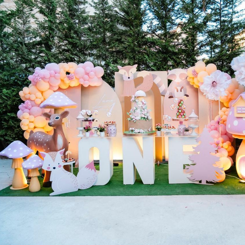 Decorative setup with balloons, letters spelling 'ONE', and cartoon characters on a grassy area.
